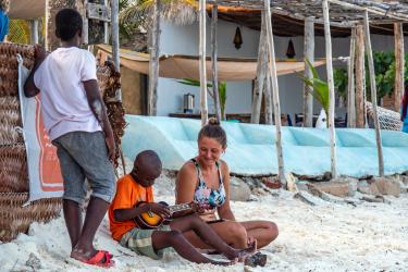 Mulher na praia ouvindo crianças a tocar viola